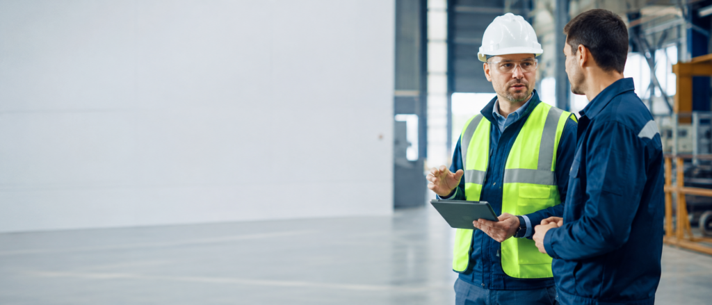 Profissional de Segurança do Trabalho orientando trabalhador em ambiente industrial.